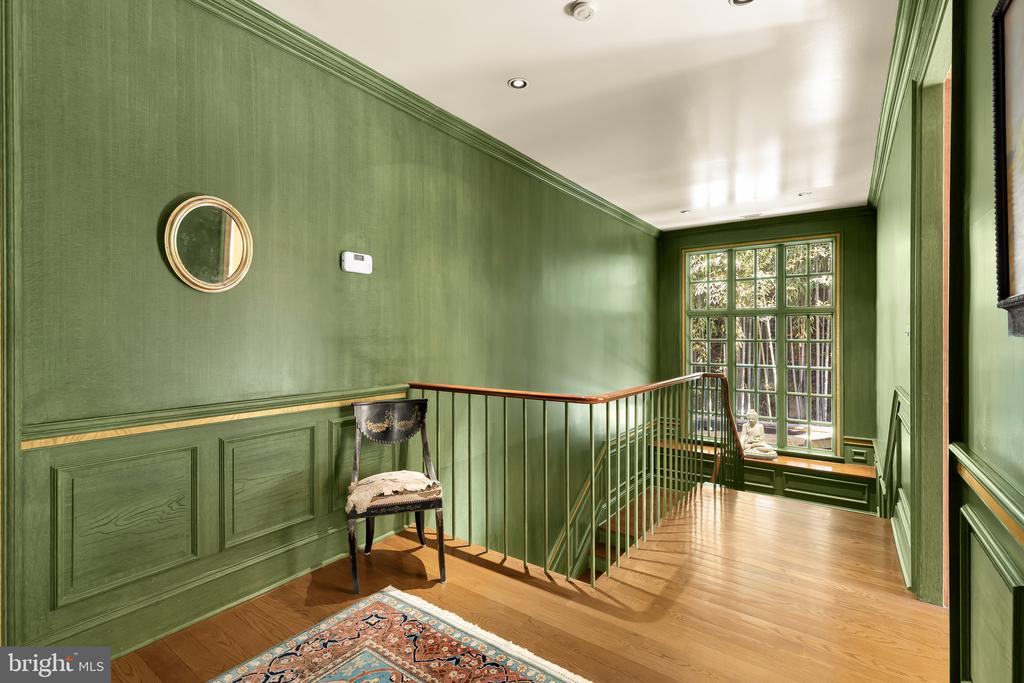 Green-paneled landing with hardwood floors, stair railing, and a large multi-pane window.