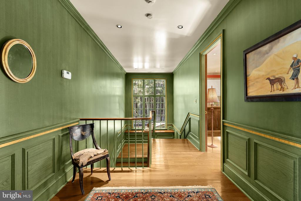 Green-paneled hallway and stair landing with hardwood floors, a tall window, and framed artwork.