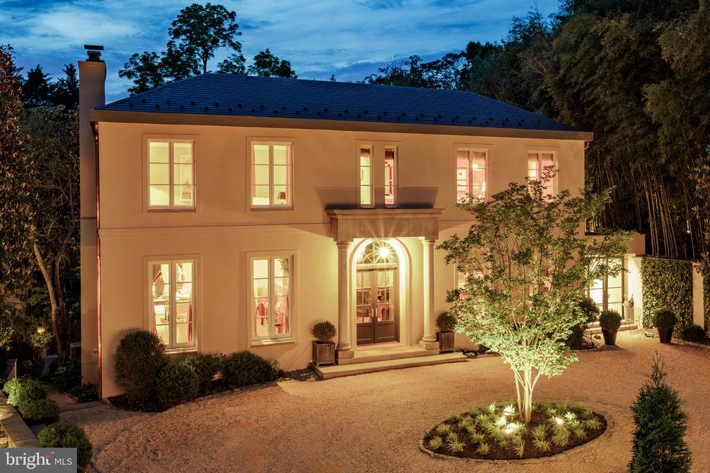 Two-story home at dusk with a lit arched entrance and landscaped gravel driveway.