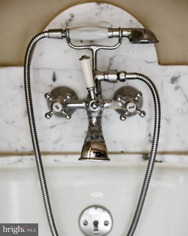 Chrome bathtub faucet and handheld shower against white marble tile, with separate hot and cold handles.