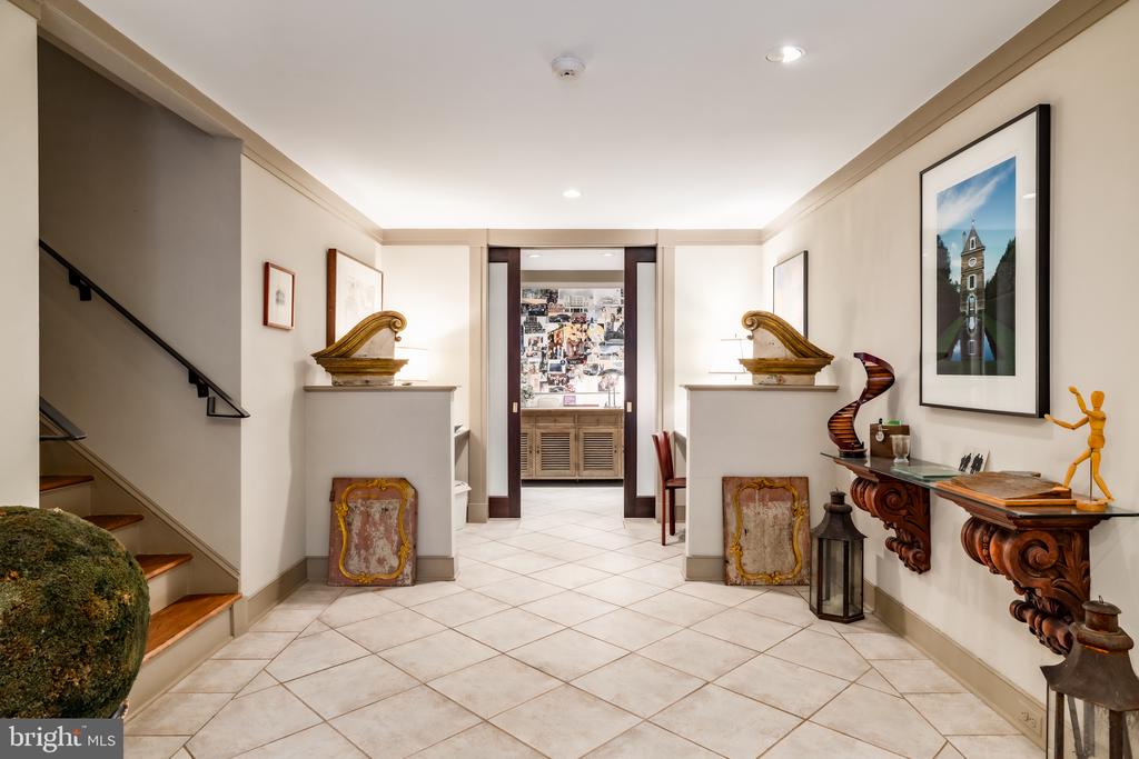 Foyer with a tiled floor, staircase, decorative consoles, and framed artwork.