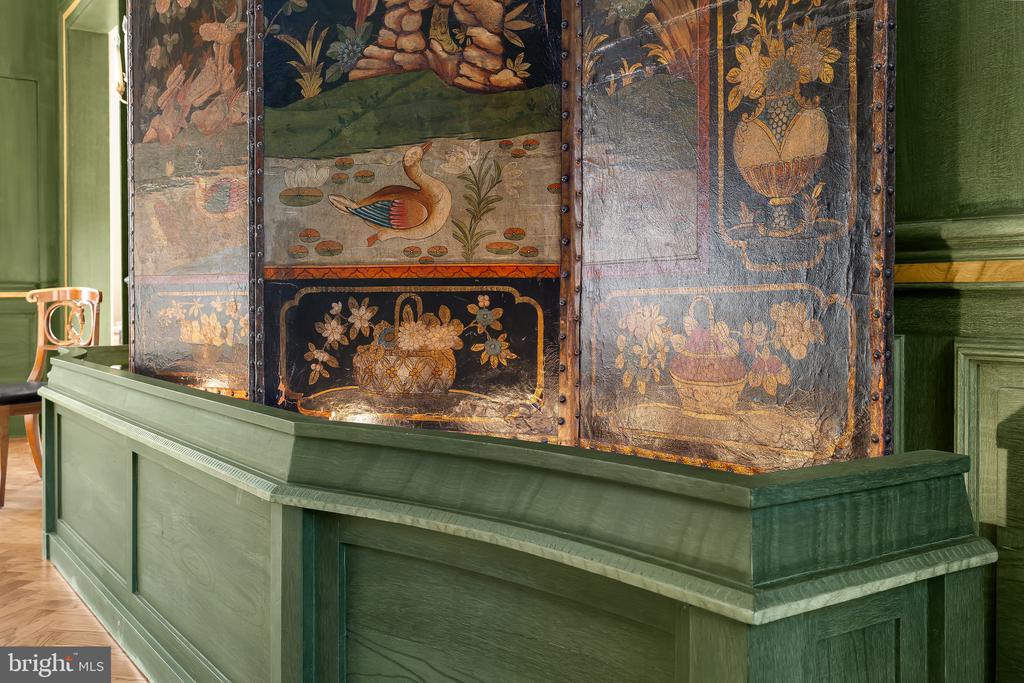 Green paneled counter in front of ornate painted panels with floral designs and a bird.