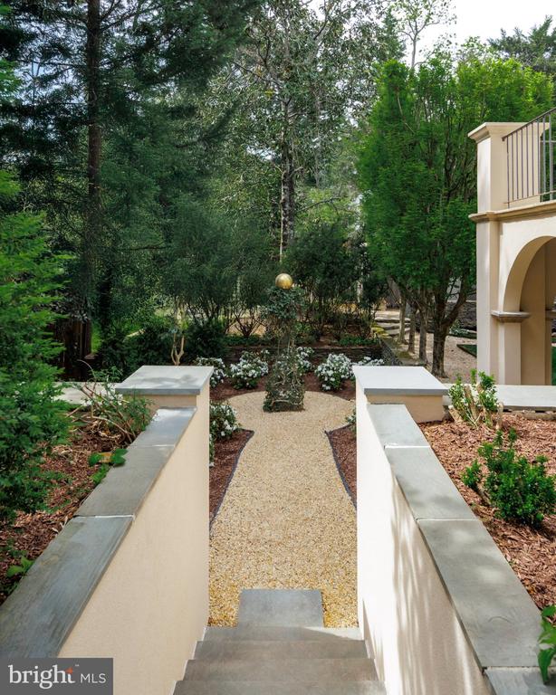 Garden entrance with a gravel path, stone steps, mature trees, and an arched balcony structure.