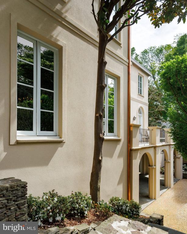 Stucco home exterior with tall windows, a mature tree, and arched covered driveway openings.