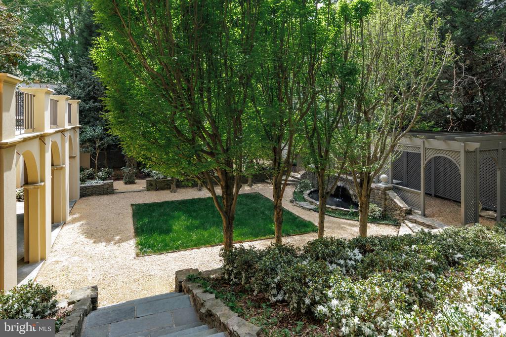 Landscaped courtyard with a central lawn, mature trees, gravel paths, stone steps, and a small pond.