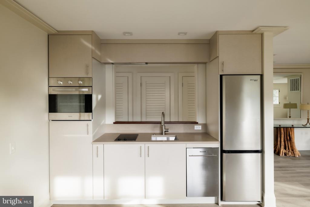 Compact modern kitchen with pale cabinets, stainless-steel appliances, and a taupe countertop.