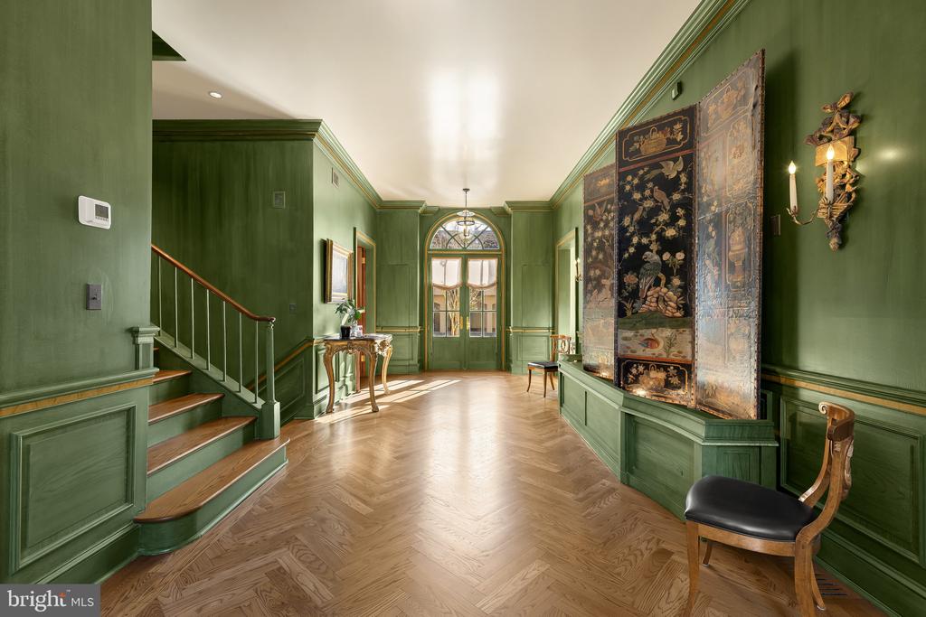 Green entry hall with a herringbone floor, staircase, ornate panels, and sunlit glass doors.