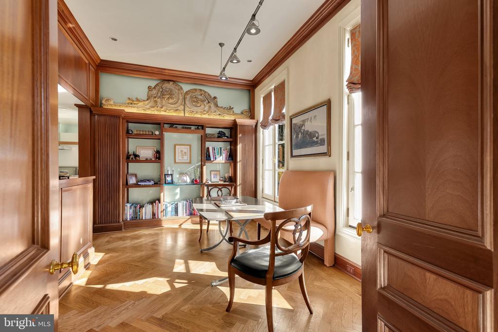 Wood-paneled home office with built-in bookshelves, a desk, and patterned parquet flooring.