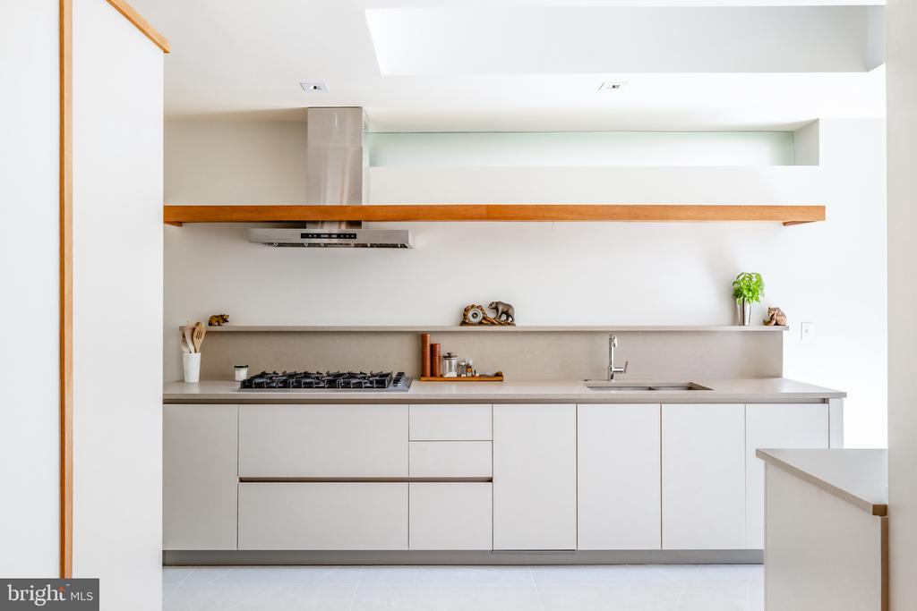 Modern white kitchen with handleless cabinets, gas cooktop, and a long wood accent shelf.