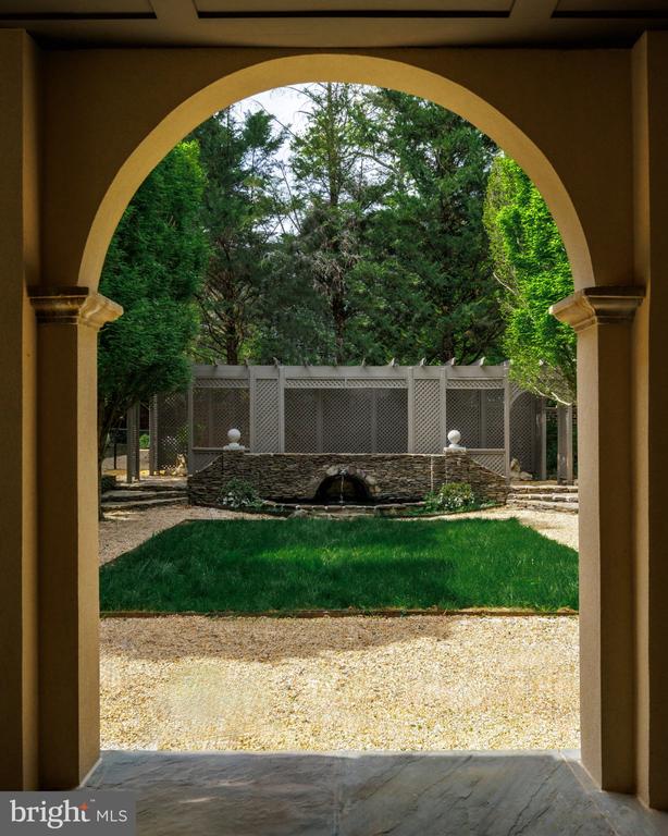 Arched porch frames a backyard lawn, stone fountain, lattice fence, and mature trees.