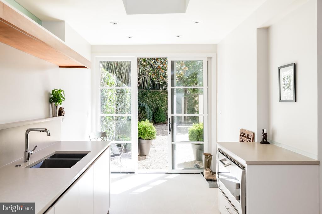 Modern white kitchen with a black sink and sliding glass doors opening to a landscaped courtyard.