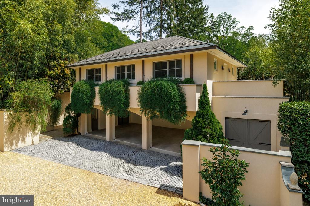 Pale stucco home with climbing greenery, covered parking, and a curved cobblestone driveway.