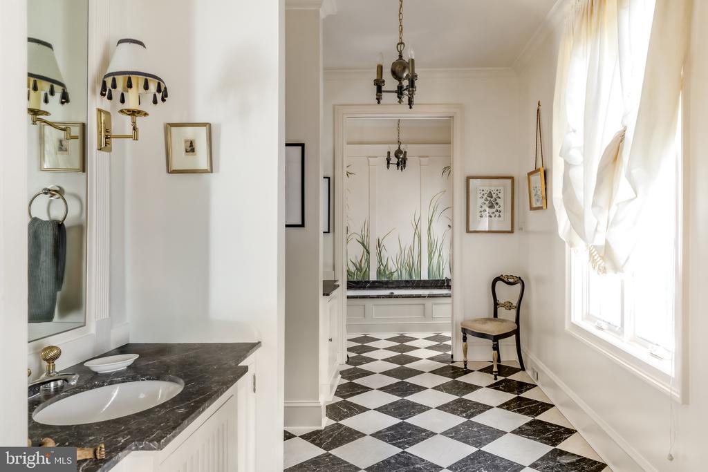 Bathroom vanity with dark marble countertop beside a black-and-white checkerboard hallway.