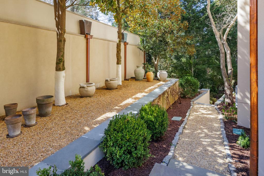 Landscaped garden courtyard with a gravel path, potted trees, and low stone edging.