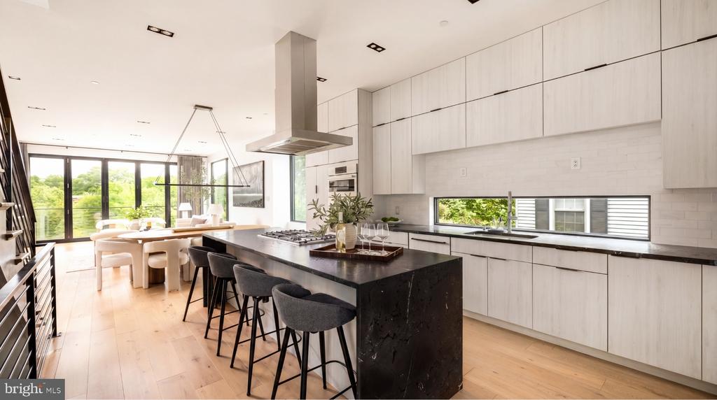 Modern kitchen with a black stone island, pale cabinetry, and windows overlooking greenery.