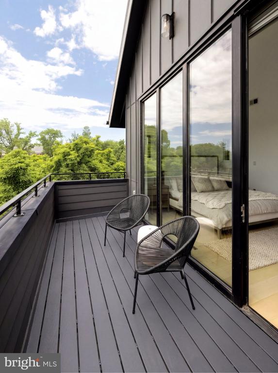 Modern balcony with woven chairs overlooks leafy trees beside sliding glass doors to a bedroom.