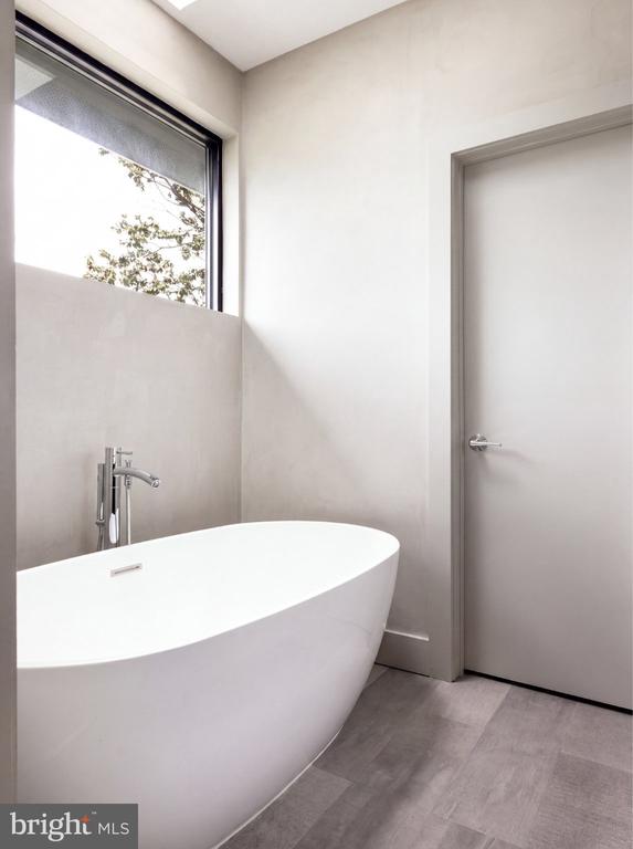 Modern bathroom with a freestanding tub beside a large window and gray tile floor.