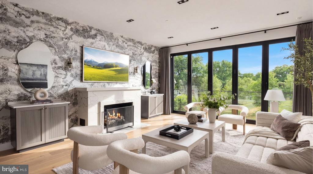 Living room with a marble fireplace wall, sculptural chairs, and glass doors overlooking greenery.