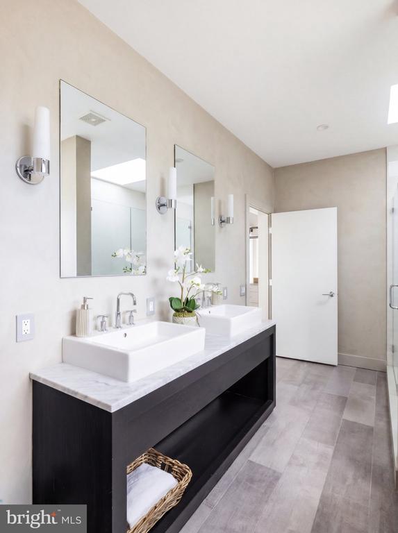 Bathroom with a dark double vanity, white vessel sinks, large mirrors, and gray tile flooring.