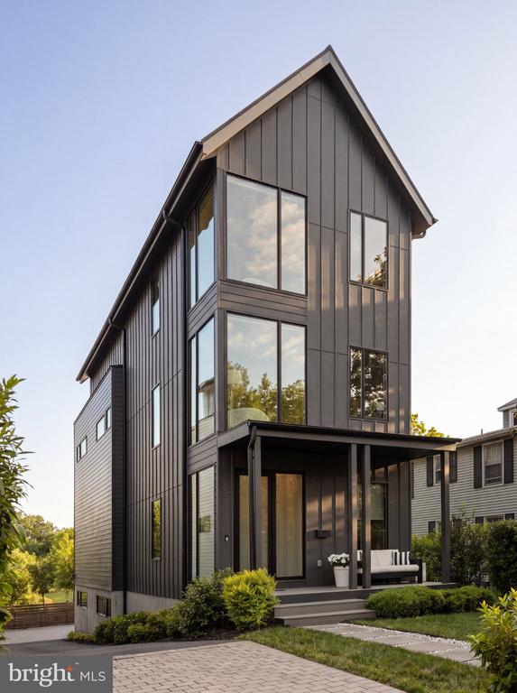 Modern dark-sided home with tall windows, a covered porch, and landscaped front yard.