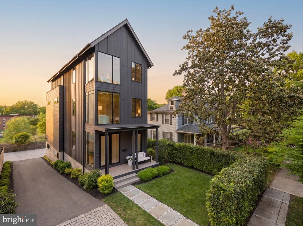 Modern dark-sided home with a covered porch, landscaped lawn, and long driveway at golden hour.