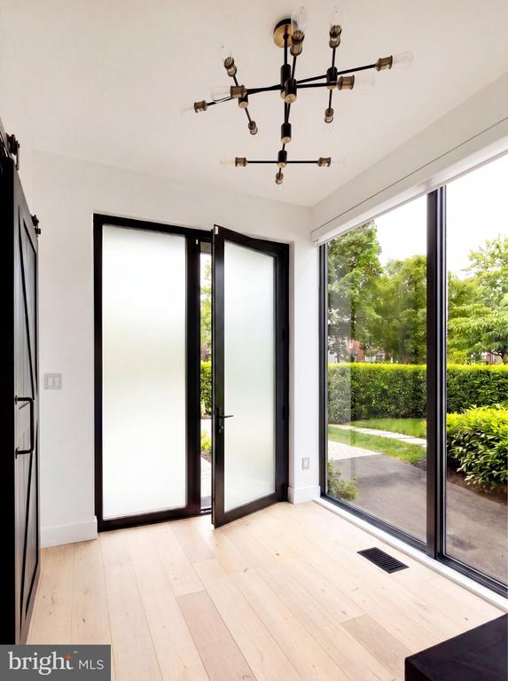 Bright interior with pale wood floors, black-framed glass doors, and windows overlooking a garden.
