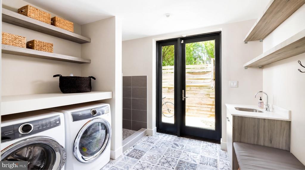 Laundry room with front-loading washer and dryer, patterned tile, utility sink, and glass doors to a fenced area.