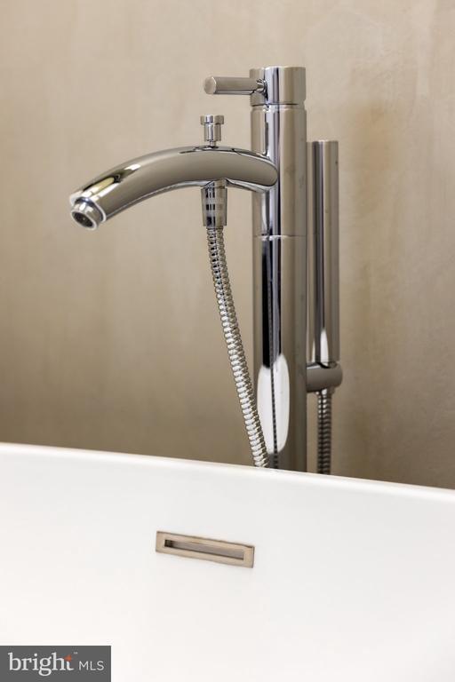 Chrome freestanding bathtub faucet and handheld shower beside a white tub.