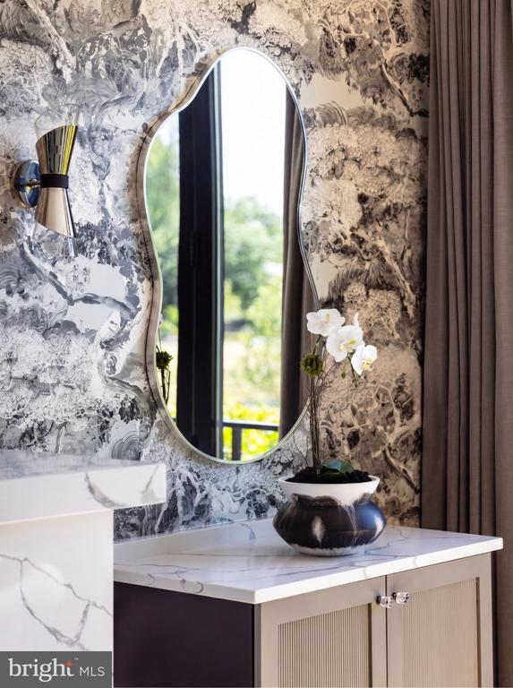 Bathroom vanity with an oval mirror, marble counter, patterned wallpaper, and white orchid.