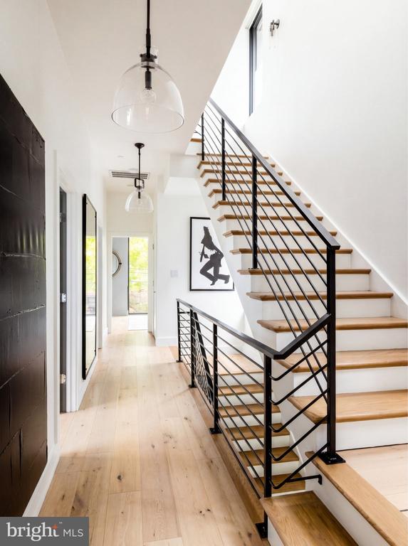 Hallway with a tall open staircase, pale wood floors, black railings, and a dark front door.