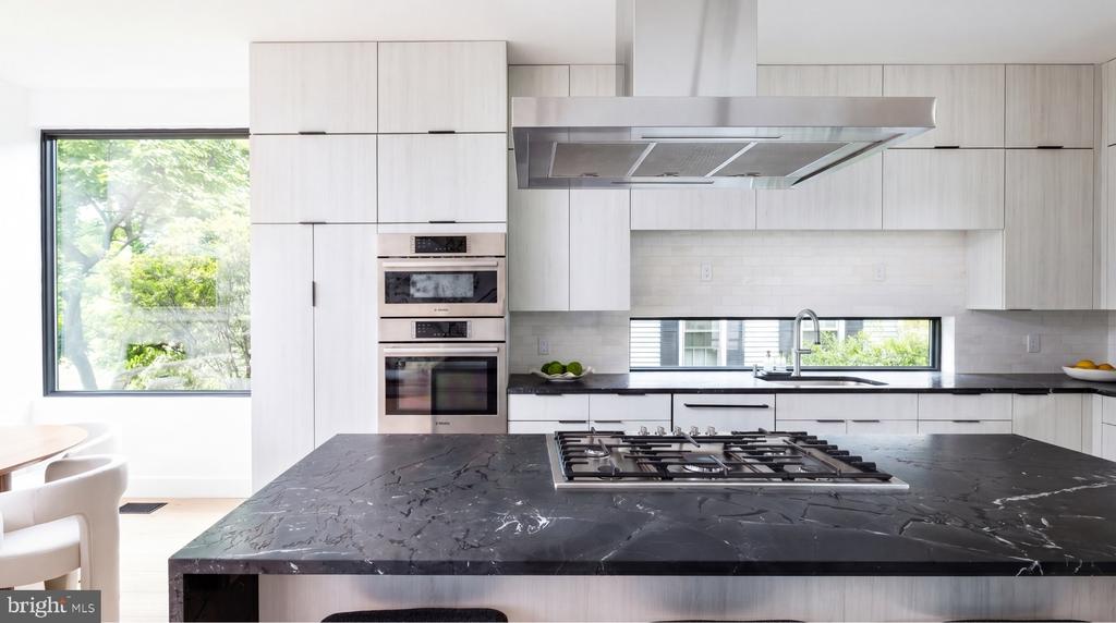 Modern kitchen with a dark marble island, gas cooktop, and white cabinetry.