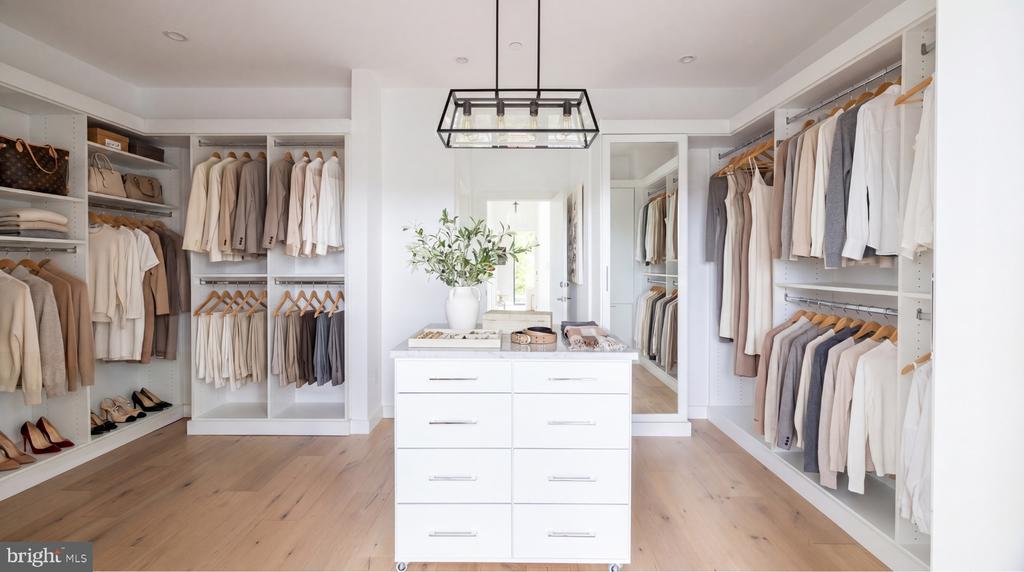 Walk-in closet with a central drawer island, white built-ins, and neatly arranged clothing.