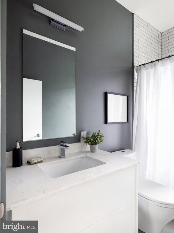 Modern bathroom with a marble-look vanity, large mirror, charcoal wall, and white-tiled shower area.