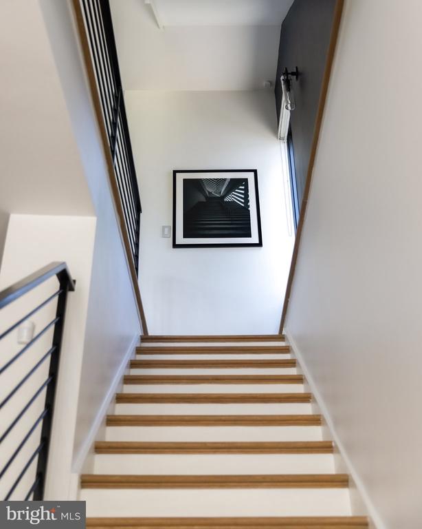 White staircase with wood-trimmed treads, black metal railing, and framed black-and-white photograph.