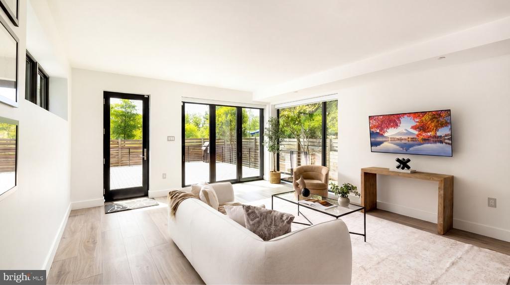 Living room with a white sofa, glass coffee table, and black-framed doors opening to a deck.