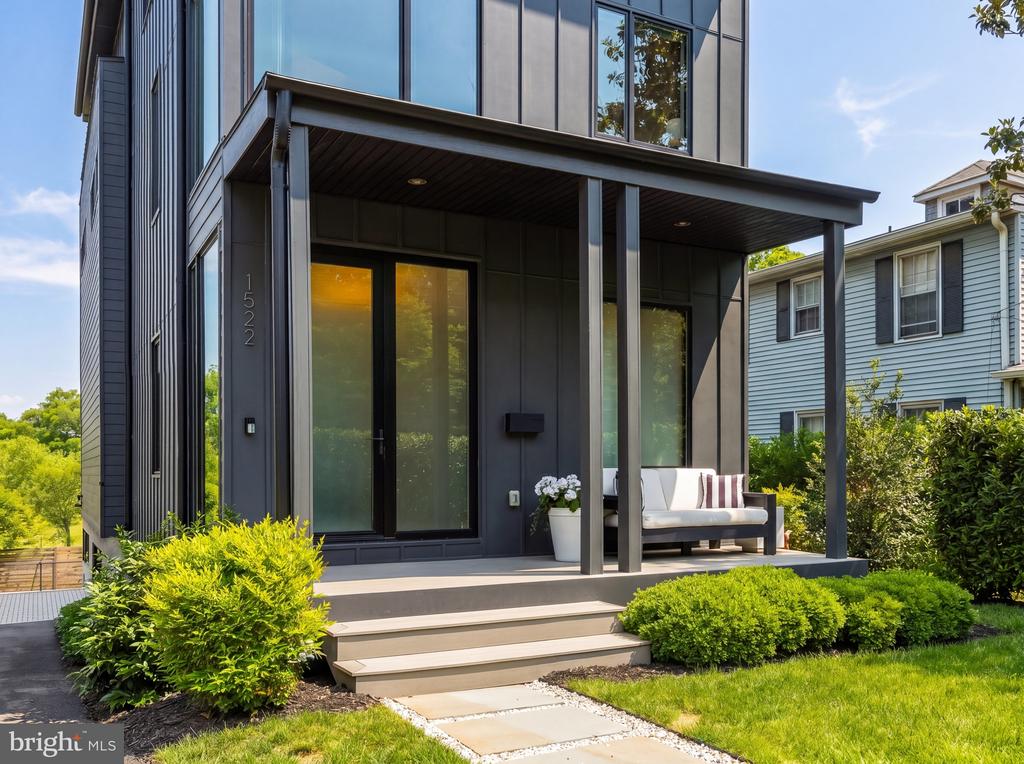 Modern dark-sided home with a covered porch, glass doors, outdoor sofa, and landscaped front yard.