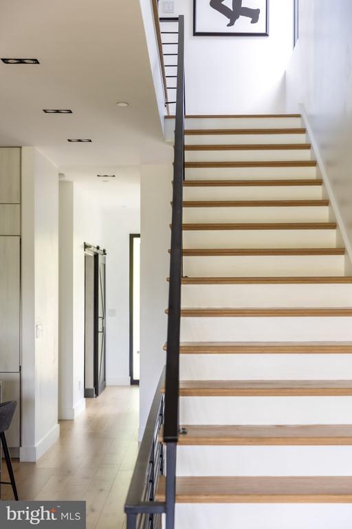 Modern staircase with wood treads and dark metal railing beside a bright hallway.