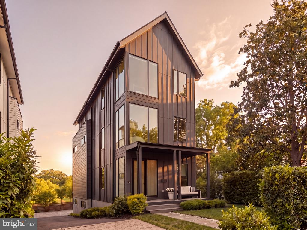 Modern dark-sided home with tall windows, a covered porch, and landscaped front yard at golden hour.