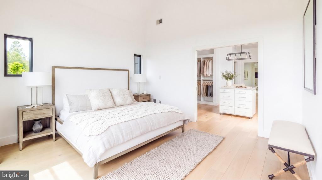 Bright bedroom with a white bed, pale wood floors, and an open doorway to a walk-in closet.