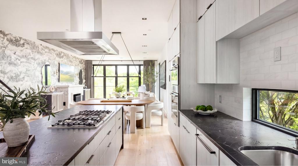Modern kitchen with dark stone counters, gas cooktop island, and wide window overlooking greenery.