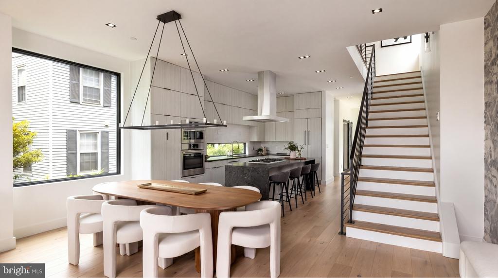 Modern kitchen and dining area with a large island, long table, and open staircase.