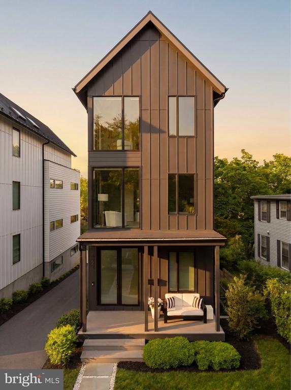 Contemporary home with a steep peaked roof, bronze siding, and a covered patio with seating.