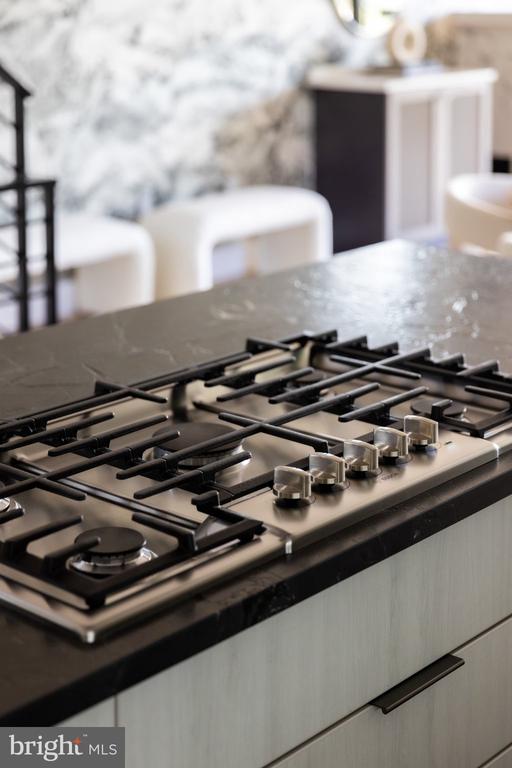 Kitchen gas cooktop set into a dark stone island with stainless-steel controls.