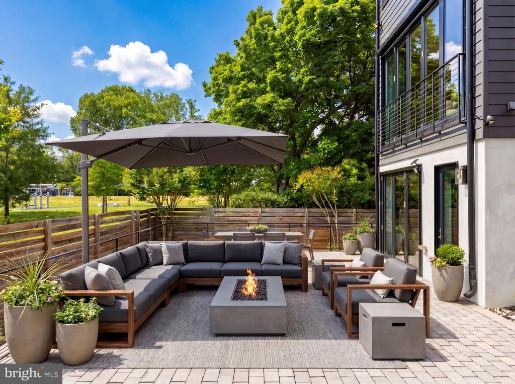 Furnished patio with sectional seating, fire table, umbrella, and fenced garden beside a modern home.