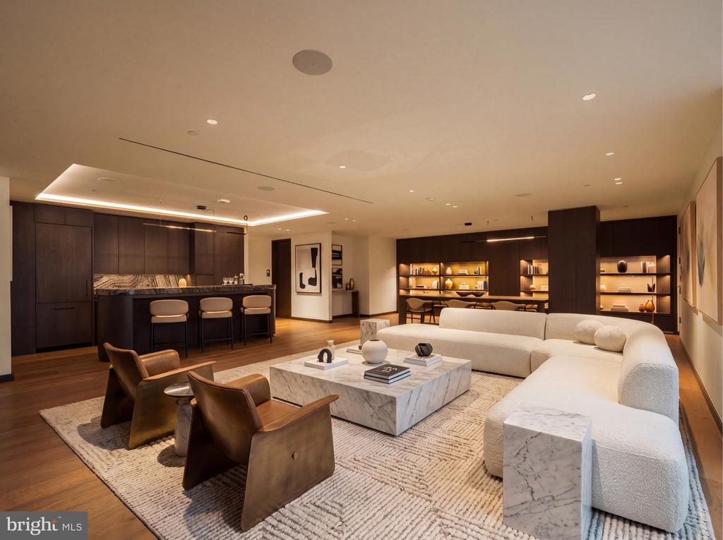 Living room with a white sectional, brown leather chairs, marble coffee table, and dark-wood kitchen.