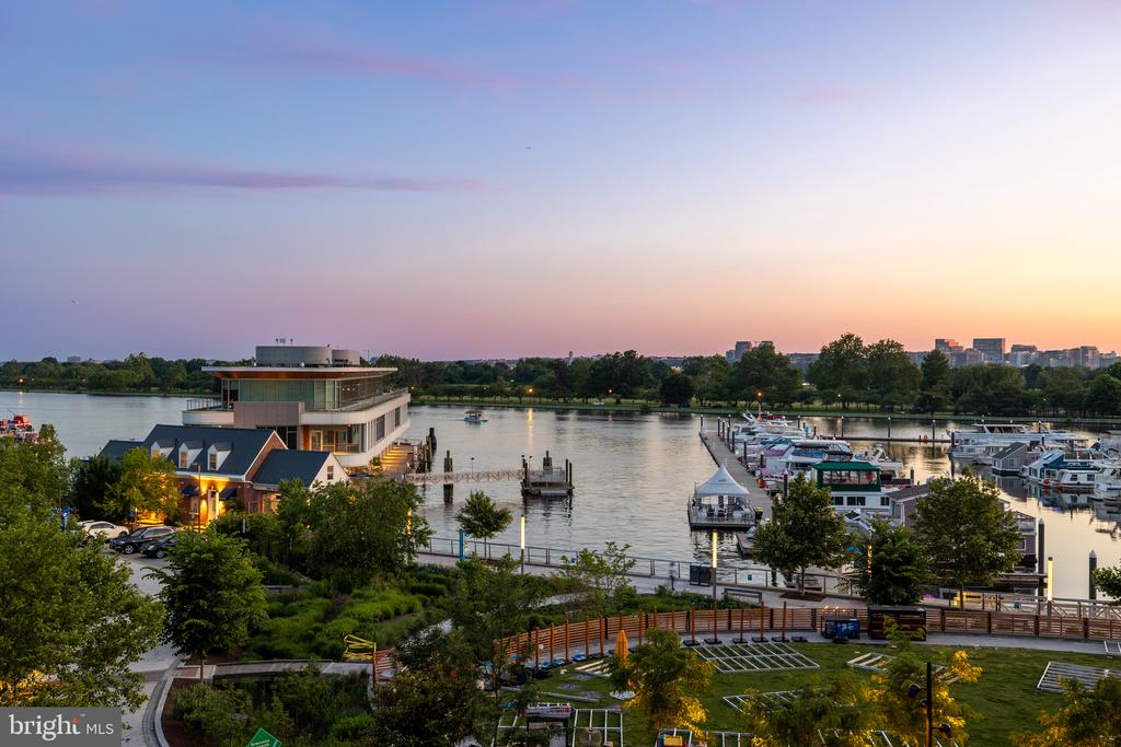 Waterfront marina at dusk, with boats, river, and distant buildings.