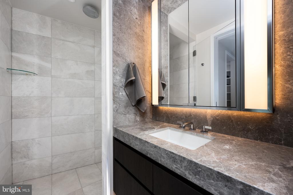 Bathroom with a gray marble vanity, illuminated mirror, and tiled shower.