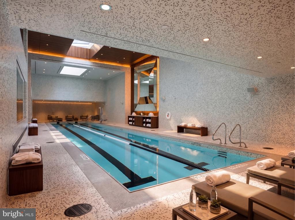 Indoor lap pool with tiled deck, cushioned loungers, and a wood-accented seating area.