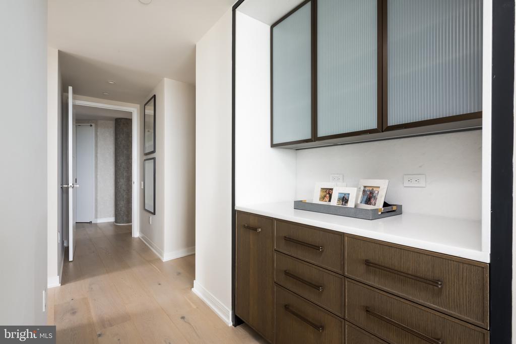 Hallway with dark wood built-in cabinetry, frosted-glass cabinets, and light wood flooring.