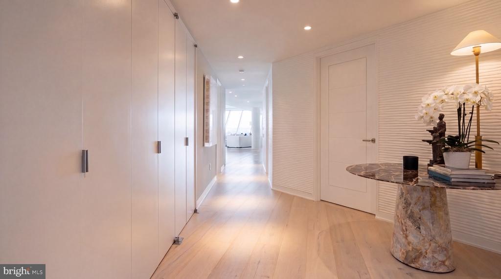 Condominium hallway with pale wood floors, built-in closets, and a marble console table topped with white orchids.